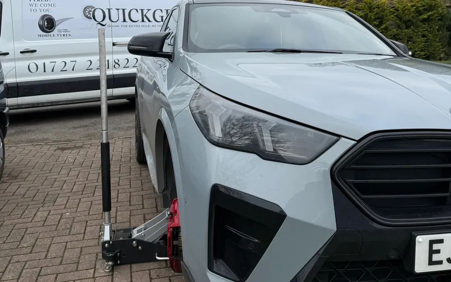 Grey crossover SUV jacked up by a QuickGrip technician, branded van behind